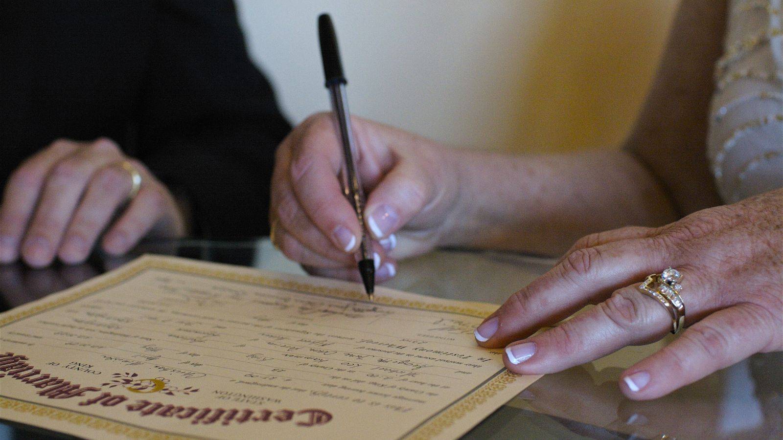 Person signing marriage certificate with wedding rings representing essential documentation for marriage visitor visa UK requirements 2025 applications