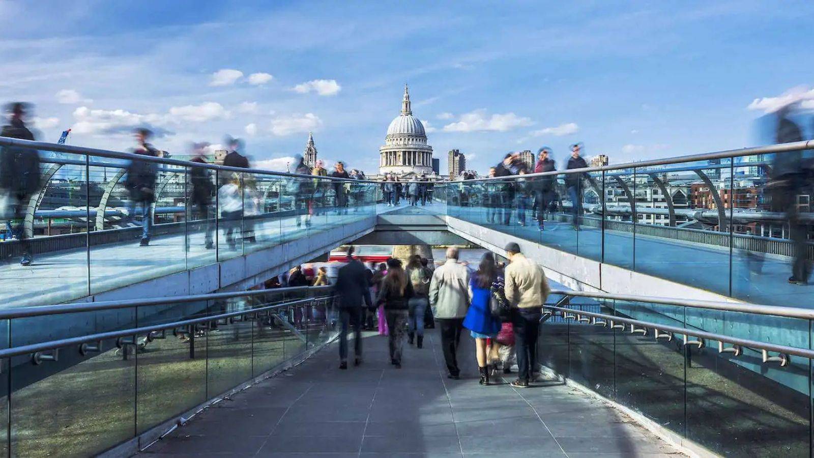 People crossing Millennium Bridge toward St Paul's Cathedral London representing skilled worker visa settlement 2025 journey to permanent residence and UK integration