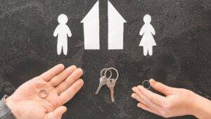 Split house model with wedding rings and property keys in separated hands representing who gets the house in a divorce UK 2025 property division disputes