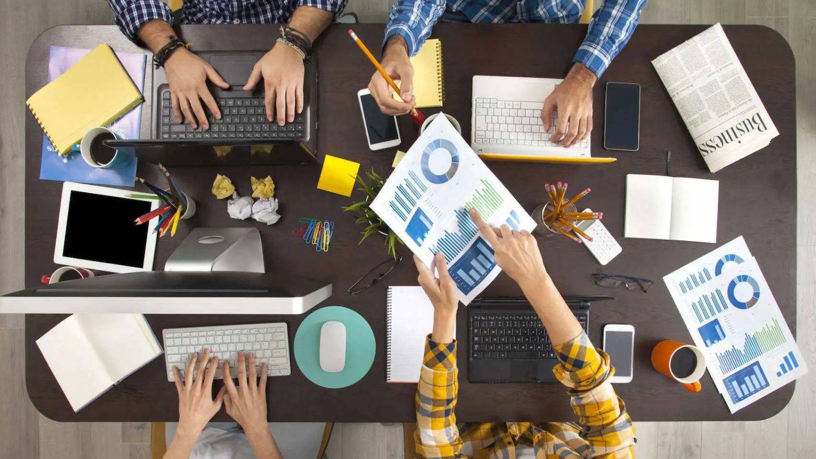 Overhead view of collaborative business team with laptops and analytics representing skilled worker visa UK 2025 professional workplace environments and sponsored employment opportunities