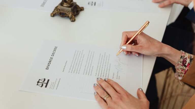 Couple signing divorce decree documents with wedding rings still on fingers and judge's gavel visible representing unreasonable behaviour divorce examples UK 2025 and historical fault-based divorce system before no-fault reform