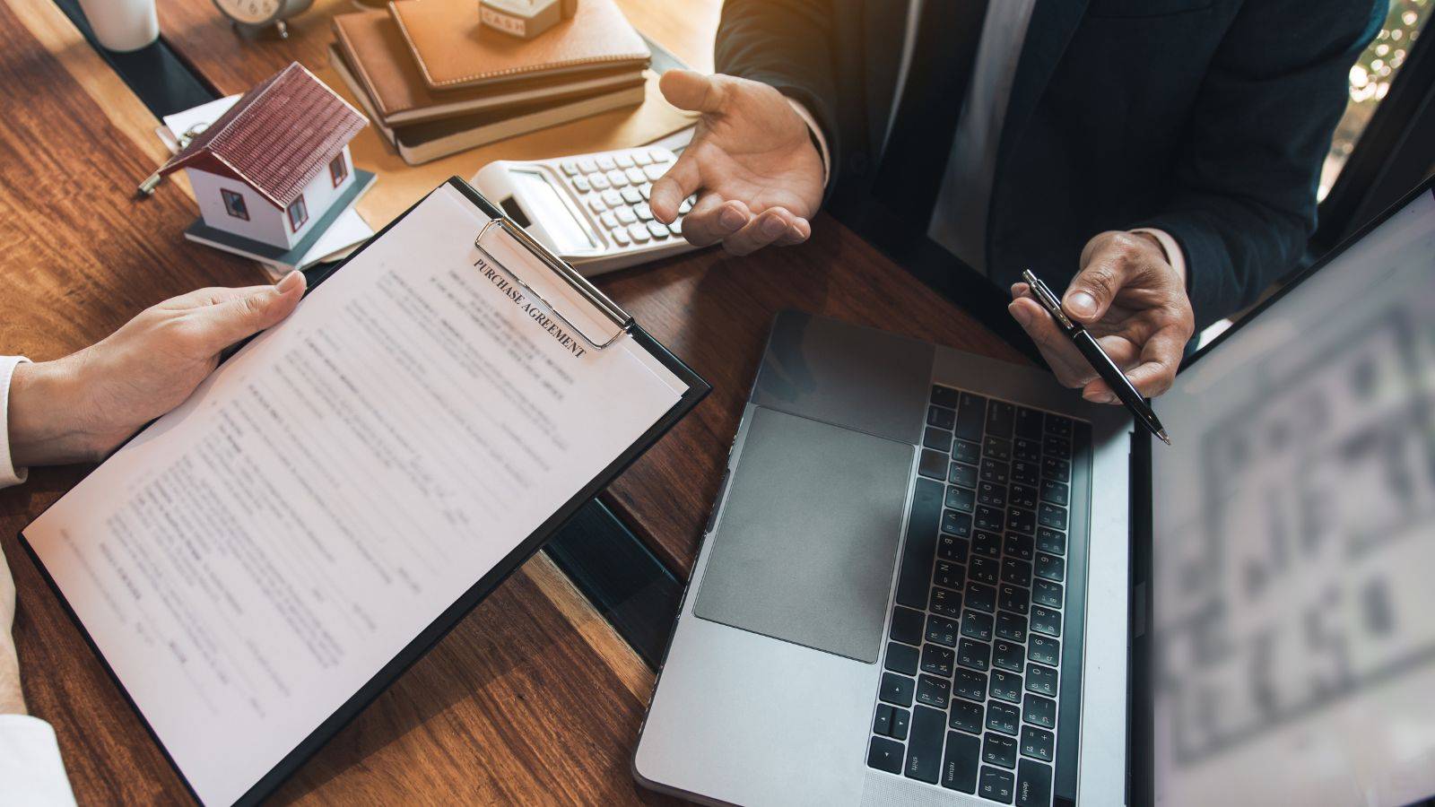 Professional signing purchase contract for freehold property with house model calculator and laptop representing purchasing freehold property UK 2025