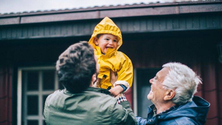 Happy grandparents lifting young grandchild in yellow raincoat outdoors representing grandparents rights UK 2026 active family contact and child arrangements