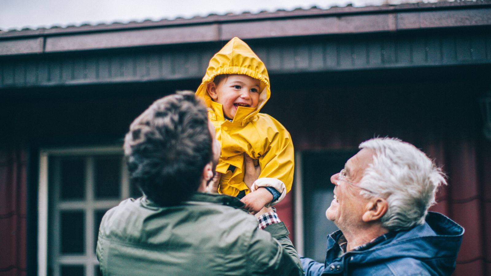 Happy grandparents lifting young grandchild in yellow raincoat outdoors representing grandparents rights UK 2025 active family contact and child arrangements