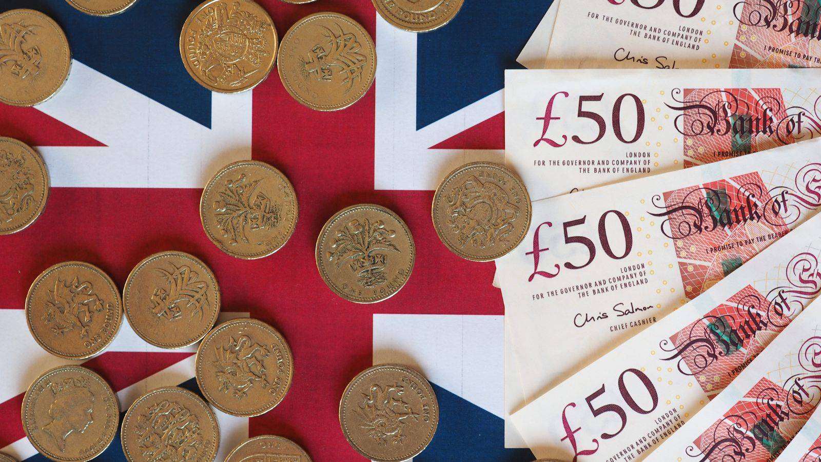 UK currency £50 notes and coins arranged on Union Jack flag representing UK spouse visa fees 2025 costs and government payments