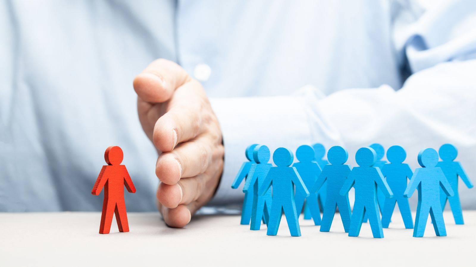 Discrimination at work solicitors UK 2025 – red figure excluded by hand from blue group representing workplace bias and protected characteristic claims.