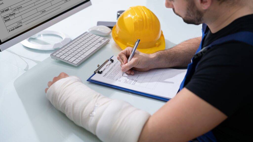 Free Tools: Injured worker with bandaged arm completing compensation calculator UK 2025 claim forms with hard hat and legal documents