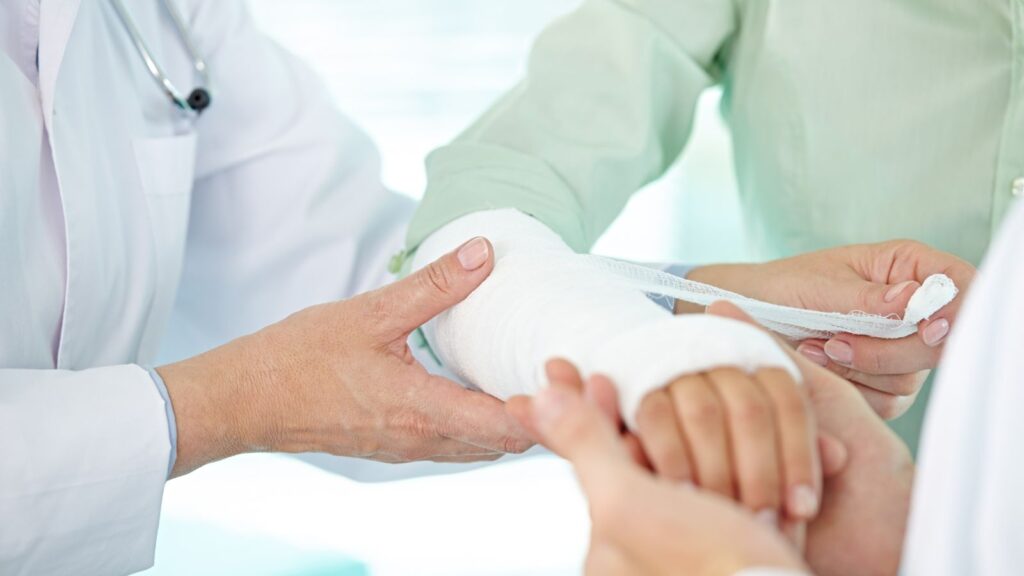 Healthcare professional doctor applying professional bandaging and cast treatment to patient's broken arm during clinical consultation for broken arm compensation UK 2025 legal claim documentation