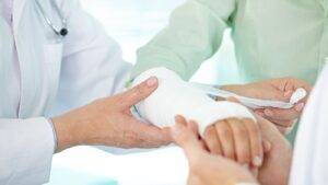 Healthcare professional doctor applying professional bandaging and cast treatment to patient's broken arm during clinical consultation for broken arm compensation UK 2025 legal claim documentation