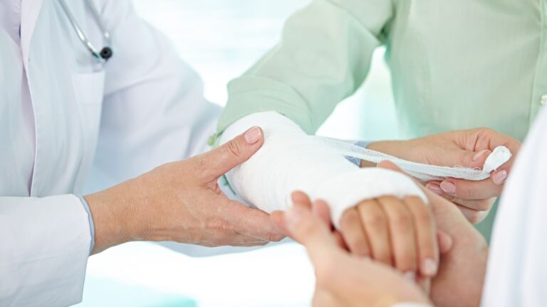 Healthcare professional doctor applying professional bandaging and cast treatment to patient's broken arm during clinical consultation for broken arm compensation UK 2025 legal claim documentation