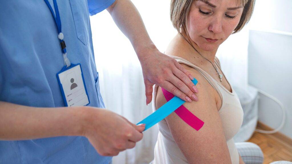 Healthcare professional physiotherapist applying blue and pink kinesiology tape to patient's shoulder during clinical assessment for shoulder injury compensation UK 2025 legal claim documentation
