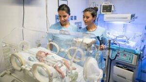 Neonatal intensive care unit showing two healthcare professionals monitoring newborn in incubator with specialized medical equipment for birth injury compensation UK 2025 medical negligence claims