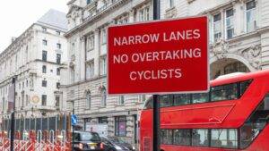 London road safety warning sign stating narrow lanes no overtaking cyclists with red bus representing cycling accident claims London 2026 borough liability and highway authority legal duties