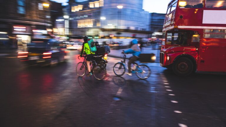 Cyclists In High-Visibility Clothing Navigating Heavy London Bus Traffic At Dusk Representing Cyclist Knocked Off Bike Compensation Uk 2026 Claims Under Highway Code Hierarchy Of Road Users Protection