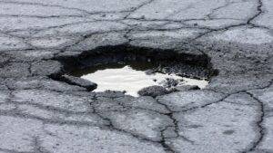 Water-filled pothole in damaged UK road surface illustrating pothole cycling accident claim UK 2026 highway defects causing injuries under Highways Act 1980 Section 41 maintenance duties